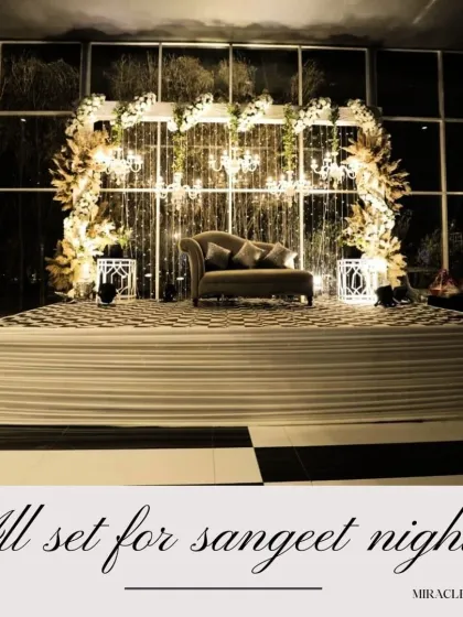 A glamorous white and gold stage setup for a Sangeet or engagement. The cascading crystals and floral arch create a look of pure elegance.