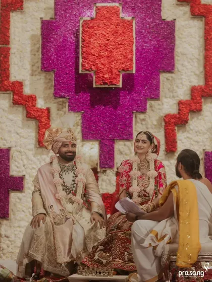 The couple seated before the priest, ready to begin their sacred rituals. The composition highlights the impressive scale of the floral backdrop, a key element of my design philosophy.