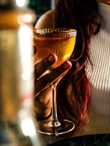 A beautifully composed shot of a woman holding a classic cocktail. The warm, golden hour lighting creates a sophisticated and relaxed atmosphere.