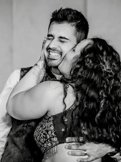 A black and white photo capturing a spontaneous, joyful kiss on the cheek. The groom's scrunched-up face and the bride's embrace show a moment of pure, playful affection.