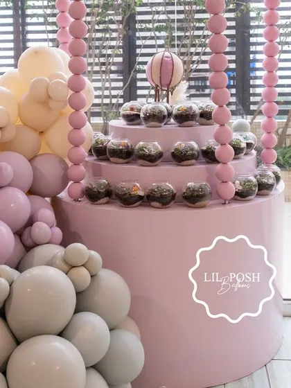 A tiered display stand for the terrarium favors, beautifully integrated with a pastel balloon garland.