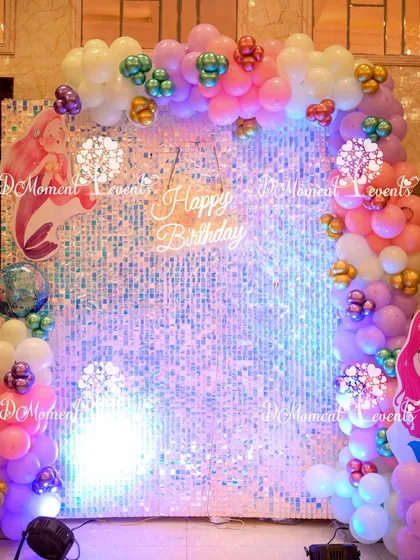 A shimmering photo backdrop made of iridescent sequins and framed with a colorful balloon arch, perfect for mermaid-themed pictures.