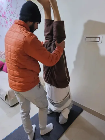 Supporting a student in a wall-assisted headstand, focusing on keeping his foundation strong and his body aligned.
