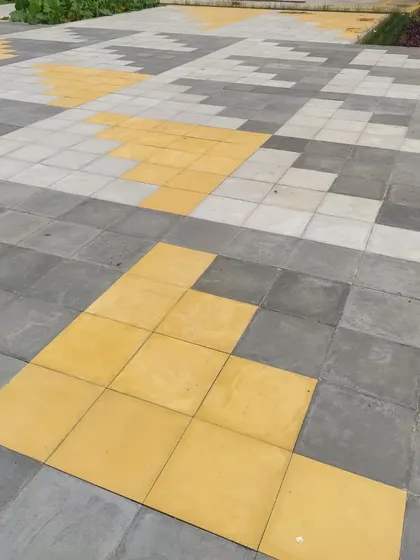 A playful pixelated pattern created with concrete pavers in shades of grey and yellow. This detail adds a touch of color and graphic interest to a large paved area in a residential layout.