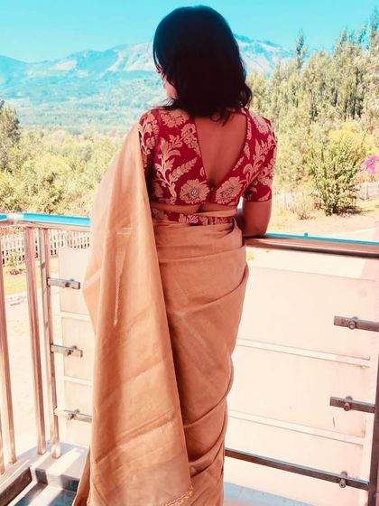 A client enjoying a scenic view, wearing a beige saree with a contrasting red brocade blouse with a V-cut back.