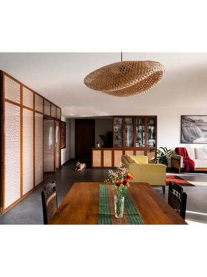 Sunlight streams into this open-plan living and dining area, highlighting the texture of the woven pendant light and the warmth of the wooden furniture.