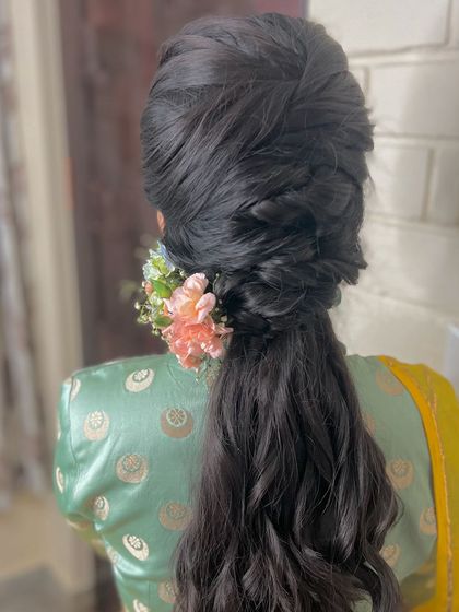A complex and voluminous braided ponytail with a floral accessory, a true statement hairstyle.