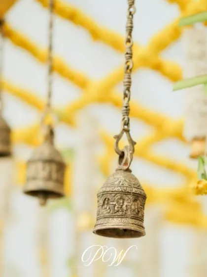 Close-up of traditional brass temple bells hanging from the mandap, adding an authentic and sacred auditory element to the ceremony.