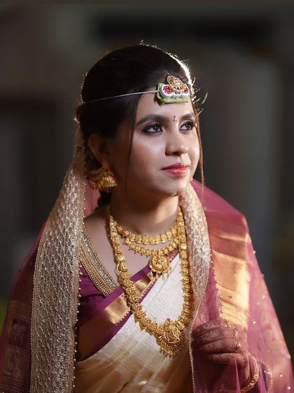 The bride during her ceremony, with a sheer veil over her head. The makeup remains visible and elegant.