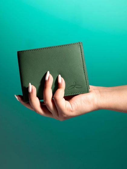 A hand holding up a green wallet against a vibrant teal background. This is a clean, straightforward product shot with a pop of color.