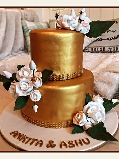 A luxurious all-gold two-tier engagement cake, adorned with clusters of white sugar roses for a truly glamorous statement.