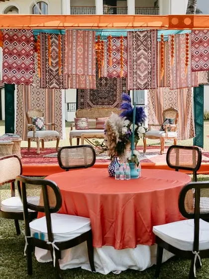 Guest seating at the Moroccan Haldi, with tables in contrasting colors of teal and rust, set against a backdrop of hanging patterned fabrics.