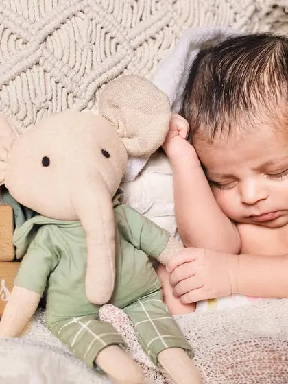 A 16-day-old newborn snuggling with a soft elephant toy. Using props like stuffed animals can help show the scale of how tiny your baby is.