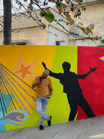 A fan poses against a colorful wall outside Shah Rukh Khan's house, "Mannat." The wall features a silhouette of SRK's iconic pose, making it a popular spot for fans to pay tribute to the Bollywood king.