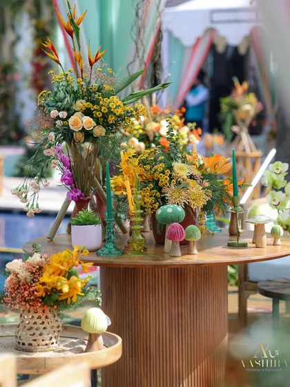 A central table laden with whimsical decor, including colorful mushroom figures and a variety of tropical and wildflower arrangements.