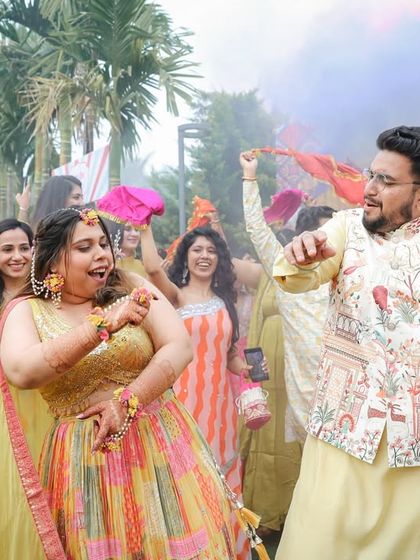 The couple dances amidst colored smoke, adding a dynamic and festive element to their Haldi celebration photos.