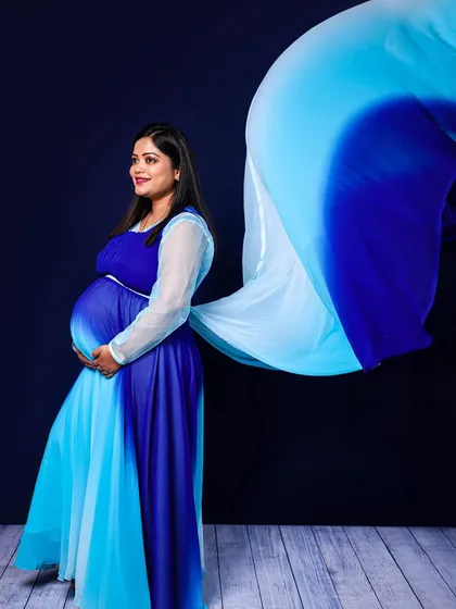 A solo portrait showcasing a beautiful dual-toned blue gown. The flowing fabric adds a sense of motion and grace, creating a timeless and artistic maternity photograph.
