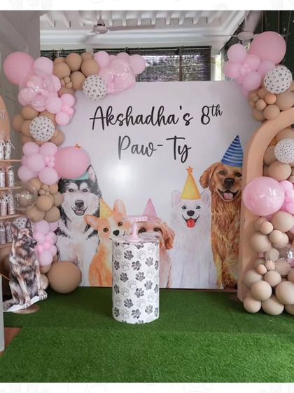 A full view of an adorable "Paw-ty" for an 8th birthday. The backdrop features illustrations of different dog breeds, and the decor includes a dog house prop and a party favor wall.