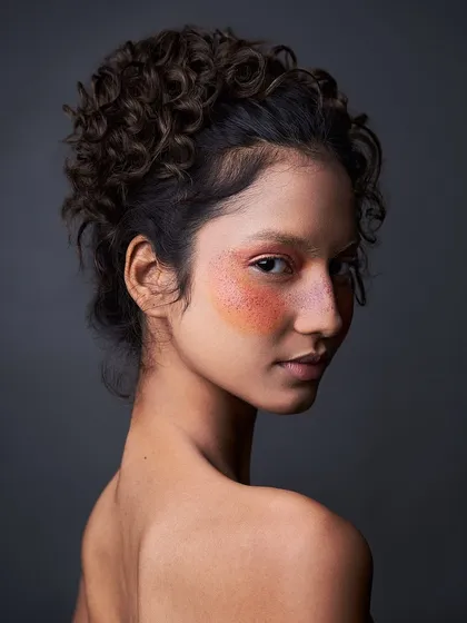 A profile view of the artistic blush look, showing the placement of color across the cheeks and nose. The curly updo adds to the renaissance-painting feel.