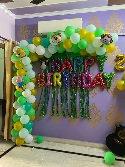 A fun jungle safari theme for a kid's birthday party at home. This setup includes a green and yellow balloon arch with animal character foils and a 'Happy Birthday' backdrop, perfect for a lively celebration.