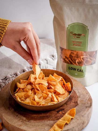 Binge on my Diet Jowar Chips instead of junk food. This image shows a hand picking a chip from a bowl, representing a smart and healthy snacking choice.