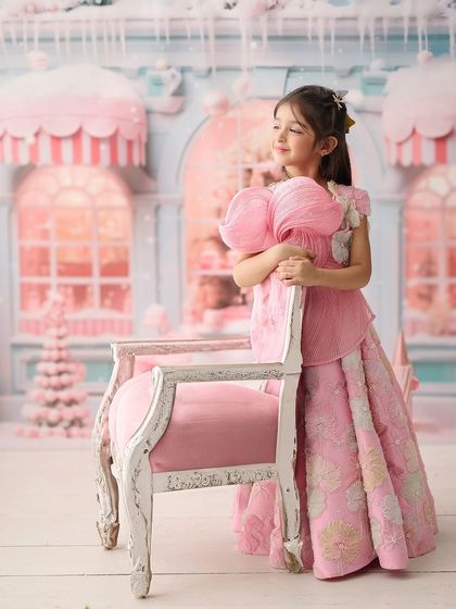 This portrait is set in a pastel-pink, candy-themed wonderland. The elaborate background and the girl's elegant pose create a stunning, high-fashion look for a children's photoshoot.