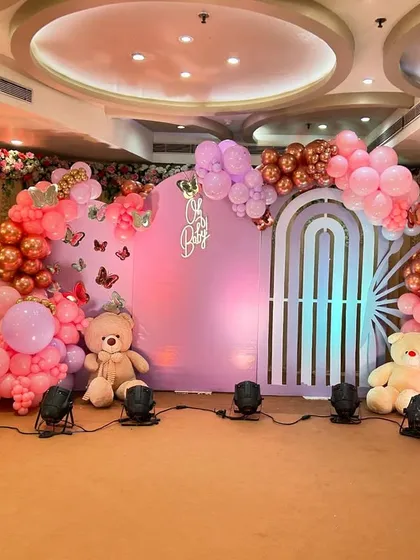 A grand 'Oh Baby' shower with a butterfly theme. This stage features a large pastel purple backdrop, butterfly wing-shaped balloon arrangements, and cute teddy bears for a whimsical touch.