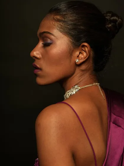 A profile view showing the sleek bun hairstyle and the subtle purple eyeshadow. This look is elegant and perfect for an evening wear photoshoot.