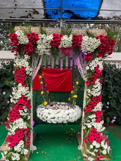 A beautiful cradle for a naming ceremony, fully decorated with red and white flowers. The simple green backdrop ensures that the ornate cradle remains the main focus.
