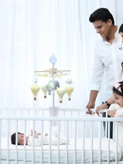 A family of four welcomes their newest member in a bright and airy lifestyle newborn session. This photo captures the whole family admiring the baby in the nursery crib.