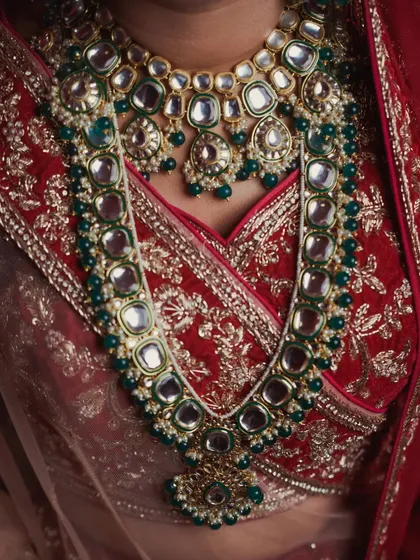 Details are the soul of a wedding's story. This close-up of the bride's kundan and emerald necklace against her embroidered red blouse highlights the exquisite craftsmanship and the care that went into choosing every element of her bridal look.