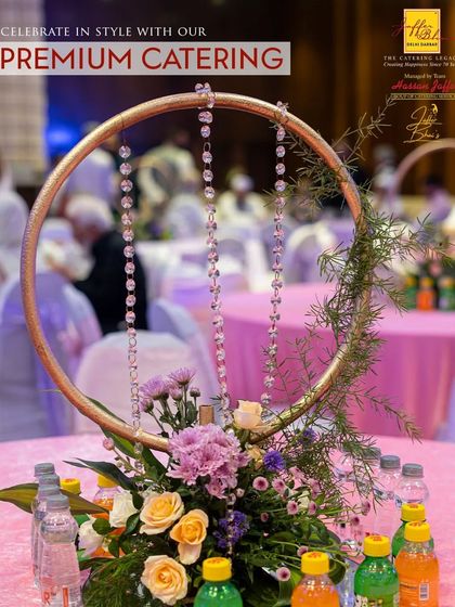 We celebrate in style with premium catering and decor. This unique tabletop centerpiece, featuring a golden hoop with hanging crystals and fresh flowers, adds a touch of modern elegance to the event's ambience.