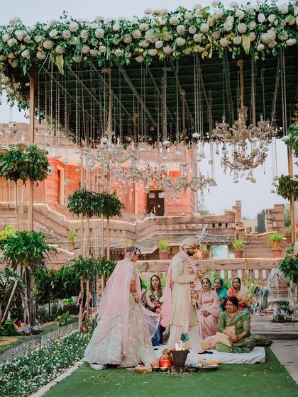 A wide shot of a beautiful outdoor Hindu wedding, showing the couple at the mandap surrounded by lush greenery and elegant decor.