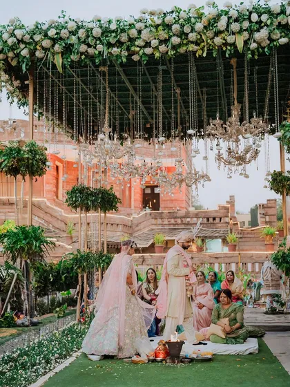 A wide shot of an opulent outdoor mandap set against a heritage building, showcasing a grand wedding setup.