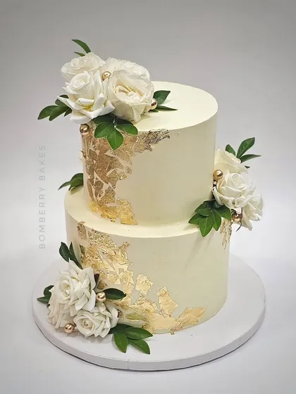A two-tier buttercream cake with white roses and gold leaf accents. This design is perfect for a chic and modern engagement party or intimate wedding.