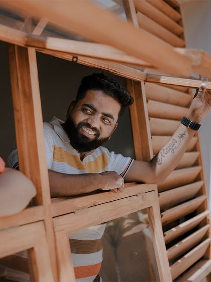 A happy, candid shot of the groom-to-be looking out a wooden window, full of anticipation.