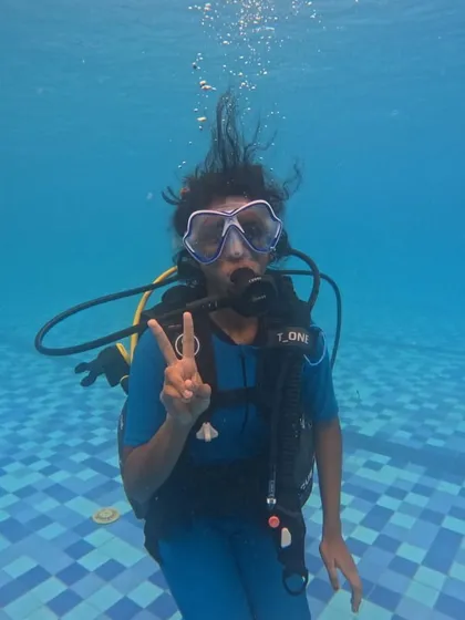 A participant flashes a peace sign, clearly enjoying her introduction to the world of scuba diving in a safe pool environment.