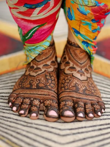 A professional photograph of the bride's feet, featuring a lovely peacock and doli design.