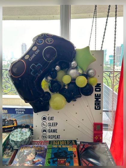 A fun and personalized "Game On" themed setup for a 40th birthday. This display includes a custom board with an "Eat, Sleep, Game, Repeat" motif and a large controller foil balloon, perfect for a gaming enthusiast.