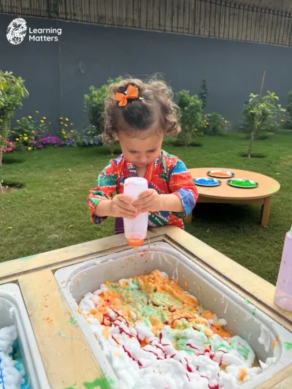 Holi celebrations are a perfect example of sensory play. Here, a child explores colored foam with a squeeze bottle, engaging their sense of touch and sight while developing the hand strength needed for writing and other fine motor tasks.