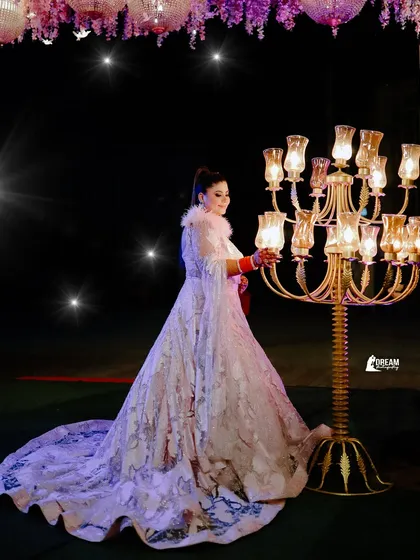 A full-length shot capturing the magnificent trail of Deepakshi's gown as she poses by a candelabra under the stars.