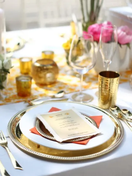 A close up of the elegant table setting for a sunny, outdoor wedding lunch. The combination of gold cutlery, silver charger plates, and a simple menu card speaks to an effortless sophistication.