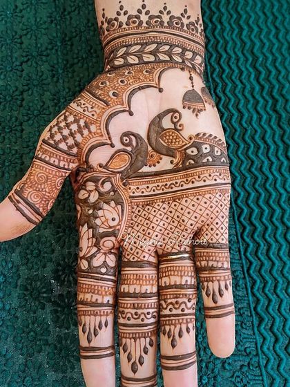 This design features two birds within a scenic panel on the hand, complete with a hanging jhumka (earring) for a playful touch.