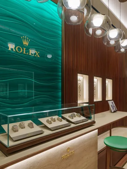 For the Rolex flagship boutique in Mumbai, we translated the brand's 119-year legacy into a physical space. The design uses a restrained palette of warm wood, travertino cladding, and the signature Rolex green to create an atmosphere of timeless elegance and refinement.
