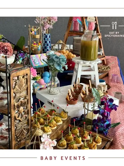 A colorful and fun grazing table designed for a baby event. The setup includes mini vada pavs, fresh juices, and a variety of other easy to eat snacks, all presented with bright, cheerful decor.