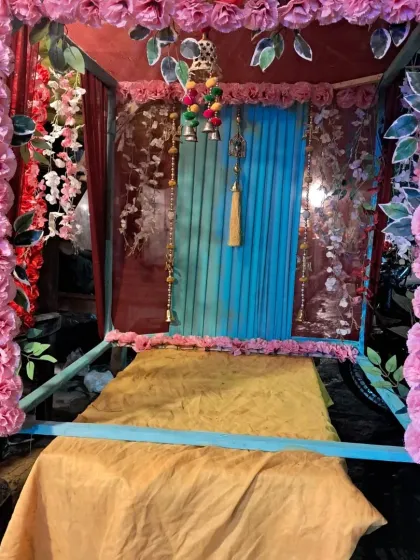 This is a small mandap or jhoola setup perfect for placing an idol during a festival. The structure is framed with pink and red artificial roses and includes a decorated seat and backdrop.