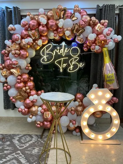 We design stylish photo booths for pre-wedding functions. This 'Bride to Be' setup includes a circular balloon frame in rose gold and white, a custom neon sign, and a light-up marquee ring prop for the perfect pictures.