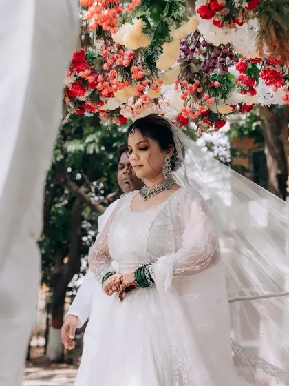 The bride's entrance under a floral canopy, looking ethereal in her white lehenga and veil.