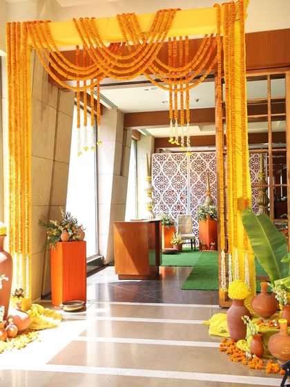 An entrance designed for a South Indian themed Haldi ceremony. Garlands of marigolds create an auspicious archway, complemented by banana leaves and terracotta pots for an authentic and traditional welcome.
