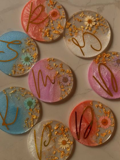 An overhead shot of the resin initial coasters. This view shows the variety of colors and how the gold calligraphy initials stand out against the floral background.